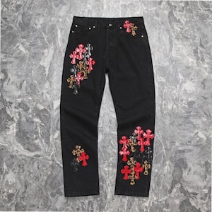 Puede incluir: Vaqueros negros con múltiples diseños bordados en forma de cruz en rojo, dorado y plateado. Los vaqueros tienen un diseño clásico de cinco bolsillos y un corte recto. Las cruces están agrupadas en la parte delantera y trasera.