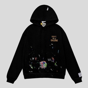 Peut inclure: Sweat-shirt &agrave; capuche noir avec un motif &eacute;clabouss&eacute; de peinture. Il pr&eacute;sente le texte "DEPT. de la GALERIE" en or sur le devant. Le capuchon porte le texte "GALLERY DEPT." en blanc. Une &eacute;tiquette est visible sur la manche.