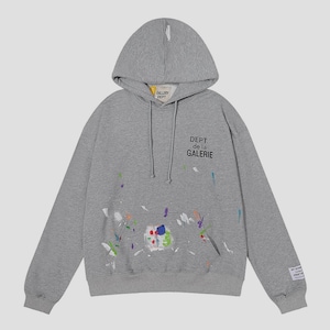 Peut inclure: Un sweat &agrave; capuche gris avec une poche avant et un cordon de serrage. Il pr&eacute;sente des &eacute;claboussures de peinture multicolores et le texte "DEPT. de la GALERIE". Une petite &eacute;tiquette est sur la manche gauche.