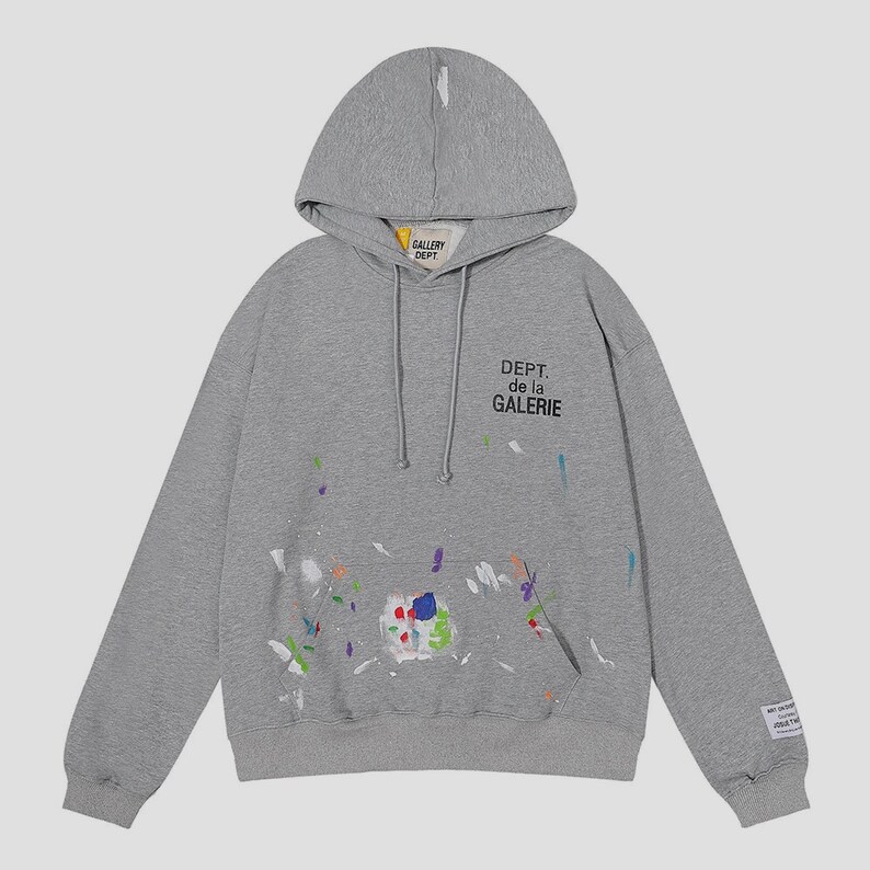 Peut inclure: Un sweat &agrave; capuche gris avec une poche avant et un cordon de serrage. Il pr&eacute;sente des &eacute;claboussures de peinture multicolores et le texte "DEPT. de la GALERIE". Une petite &eacute;tiquette est sur la manche gauche.