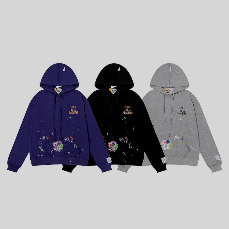 Peut inclure: Trois sweat-shirts &agrave; capuche de couleur bleu marine, noir et gris. Chaque sweat-shirt pr&eacute;sente des &eacute;claboussures de peinture multicolores et le texte "DEPT. de la GALERIE" en or. Les sweat-shirts ont une poche avant et une petite &eacute;tiquette sur la manche.