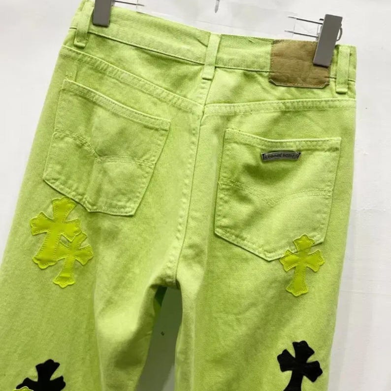 May include: Lime green denim jeans with cross appliqu&eacute;s. The jeans feature back pockets and a brown leather patch. The cross designs are in contrasting colors, with black and neon green crosses.