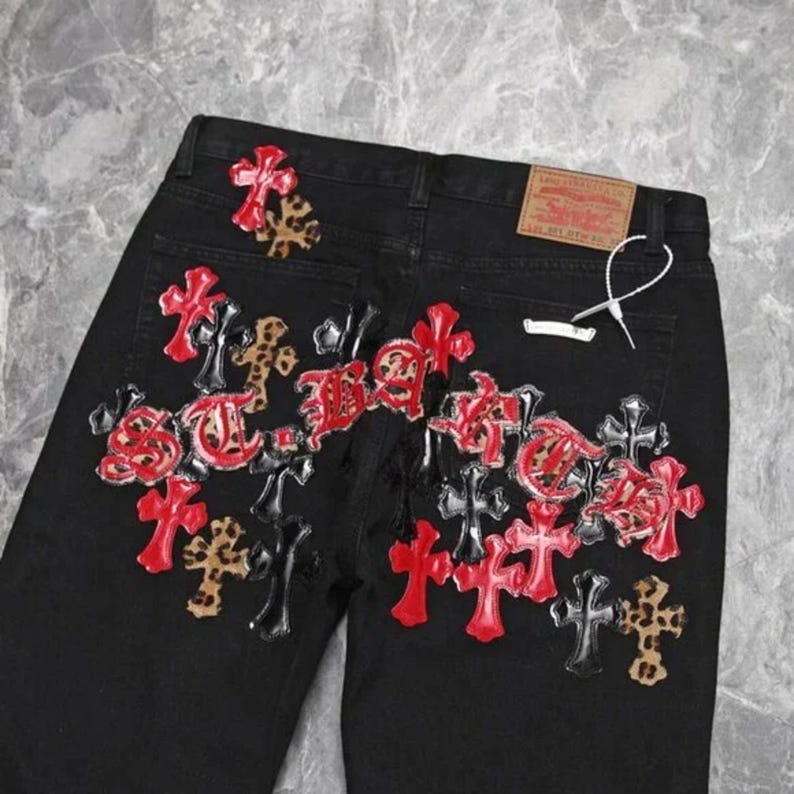 Puede incluir: Vaqueros negros con un dise&ntilde;o de cruces decorativas en rojo, negro y estampado de leopardo. Los vaqueros tienen un dise&ntilde;o cl&aacute;sico de cinco bolsillos y una etiqueta de la marca Levi's.