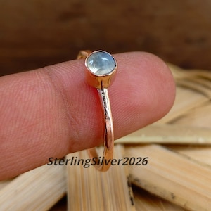 Peut inclure: Une bague couleur or rose avec une pierre cabochon bleu clair unique, sertie dans un chaton rond. L'anneau présente une finition martelée texturée. Le texte SterlingSilver2026 est visible dans la partie inférieure de l'image.