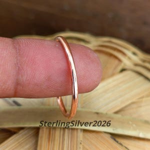 Puede incluir: Un anillo de metal fino de color cobre, pulido y con una superficie lisa y redondeada. El anillo está colocado verticalmente y muestra un acabado reflectante. El texto SterlingSilver2026 es visible en la parte inferior de la imagen.