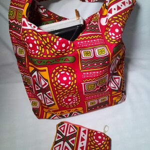 May include: A red, yellow, and white patterned tote bag with a matching zippered pouch. The tote bag has a handle and contains a black notebook. The fabric features geometric shapes and designs.