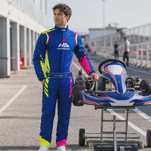 May include: A blue racing suit with neon yellow and pink side panels, featuring the white HS HISPEED logo on the chest and a belt with the text R. Costa A+. The suit includes Italian flag accents on the shoulders and a high collar design.