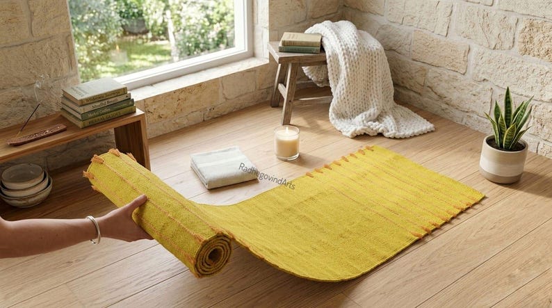 Puede incluir: Una esterilla de yoga amarilla, parcialmente desenrollada, est&aacute; sobre un suelo de madera. Una peque&ntilde;a vela, una toalla blanca doblada y una planta en maceta est&aacute;n cerca. La esterilla mide unos 183 cm de largo.