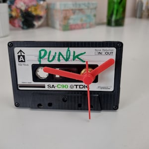 May include: A black cassette tape clock with red hands. The word "PUNK" is written in green on the tape. The cassette is a TDK SA-C90. A unique decorative item for a music lover.