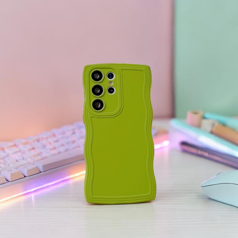 Peut inclure: Une coque de t&eacute;l&eacute;phone vert citron avec un bord ondul&eacute;. L'&eacute;tui comporte trois objectifs d'appareil photo et un flash. La coque est sur une surface blanche avec un clavier et une souris en arri&egrave;re-plan.