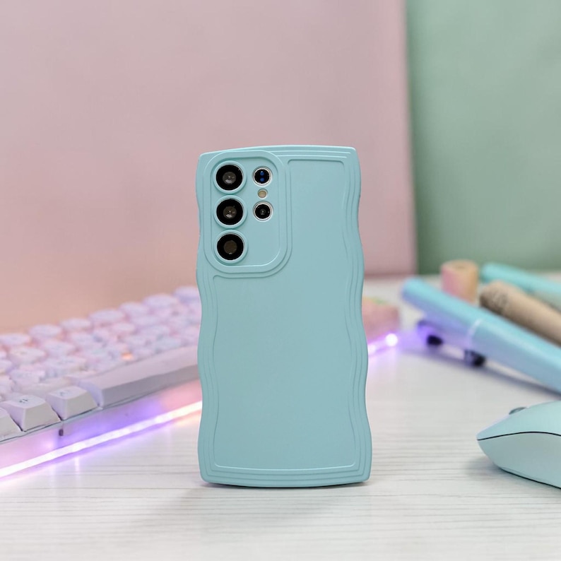 Peut inclure: Une coque de t&eacute;l&eacute;phone bleu clair avec un design &agrave; bord ondul&eacute;. L'&eacute;tui comporte un module cam&eacute;ra avec trois lentilles et un petit flash. L'&eacute;tui est fait d'un mat&eacute;riau lisse et est con&ccedil;u pour prot&eacute;ger le t&eacute;l&eacute;phone.