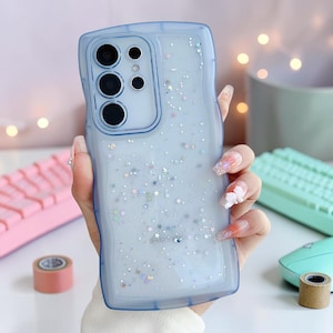 Könnte beinhalten: Hellblaue Handyhülle mit gewelltem Rand, gefüllt mit Glitzer und sternförmigem Konfetti. Die Hülle hat eine transparente Rückseite und einen blauen Rahmen, entworfen für ein Smartphone.