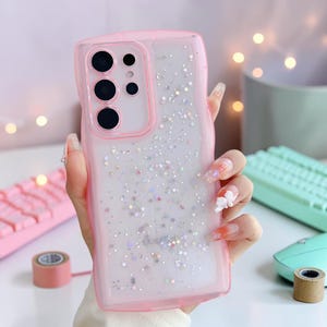 Puede incluir: Funda transparente para tel&eacute;fono con borde rosa y dise&ntilde;o de estrellas brillantes. La funda tiene una parte trasera transparente con borde rosa y dise&ntilde;o de estrellas brillantes. Dise&ntilde;ada para un tel&eacute;fono Samsung.