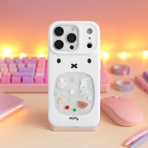 Könnte beinhalten: Weißes Handycase mit einem Cartoon-Hasen-Design. Das Case hat ein transparentes Fenster mit verschiedenen kleinen, bunten Charms, darunter Hasen, Sterne und ein Bär. Das Wort "Miffy" ist unten aufgedruckt.