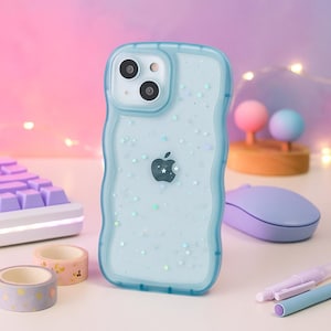 May include: A light blue phone case with a wavy edge, featuring a glittery design with small stars and an Apple logo. The case is next to a purple keyboard, washi tape rolls, and a lavender mouse.