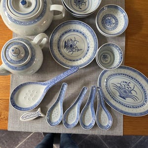 May include: A set of white and blue porcelain tableware, including teapots, bowls, plates, and spoons. The items have a blue floral and geometric pattern. A small fish-shaped dish is also present.
