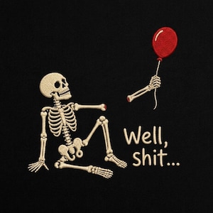 May include: An embroidered design on a black background featuring a beige skeleton sitting down with one arm detached, holding a red balloon with its detached hand. The text "Well, shit..." is embroidered in beige lettering next to the skeleton.