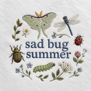 Op de afbeelding: Een witte stof met geborduurde insecten en bloemen rondom de blauwe tekst "sad bug summer". Het ontwerp bevat een lichtgroene nachtvlinder, een blauwe libel, een rood lieveheersbeestje, een bruine kever en een groene rups tussen kleine bloemetjes.