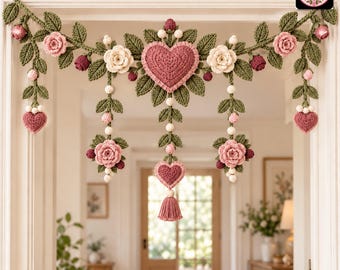 May include: A crochet garland featuring a central pink heart, cream and pink roses, green leaves, and small buds. The decorative piece includes hanging elements with additional hearts, roses, and a tassel, all crafted with intricate yarn textures.