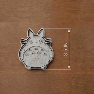 May include: A gray cookie cutter in the shape of a cartoon character, measuring 3.5 inches. The cutter features a detailed outline of the character's face, ears, and belly markings. The cutter is designed for making cookies or other treats.