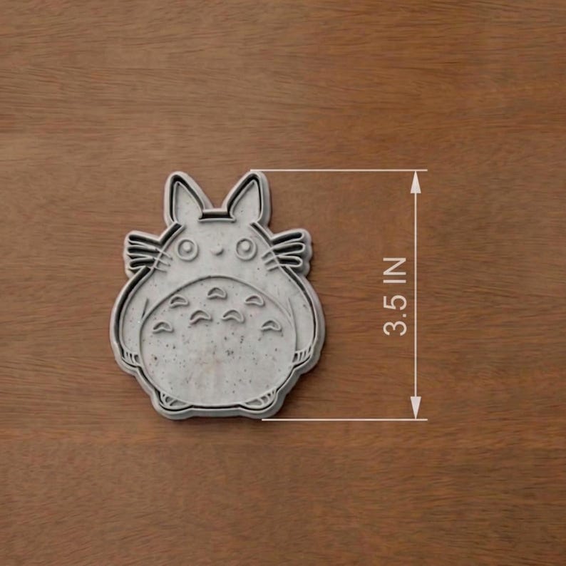 May include: A gray cookie cutter in the shape of a cartoon character, measuring 3.5 inches. The cutter features a detailed outline of the character's face, ears, and belly markings. The cutter is designed for making cookies or other treats.