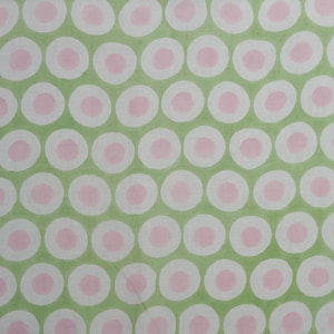May include: A fabric with a repeating pattern of white circles with pink centers on a light green background. The circles are evenly spaced, creating a visually appealing and symmetrical design. The fabric appears to be cotton or a similar material.