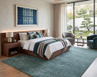 May include: A bedroom featuring a low-profile wooden bed frame with white bedding, a teal throw blanket, and patterned pillows. A large teal area rug covers the wooden floor. A framed blue and white textile art piece hangs above the headboard.