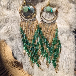 May include: A pair of long, beaded earrings with gold hoops and green and white stones. The earrings have a fringe of green and gold beads.