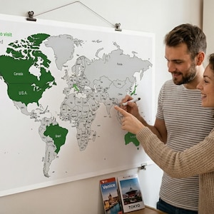 May include: A world map, with countries coloured green to show places visited and green for places desired to visit. A couple is shown pointing at the map with a marker. The map is hanging on a wall.
