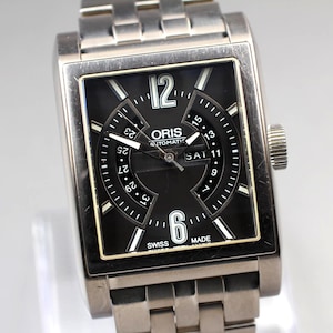 May include: A stainless steel Oris automatic watch with a black square face. The watch features white numerals and hands, a date display, and the text "SWISS MADE". The watch band is also stainless steel.