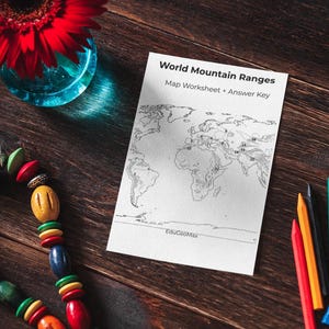 Puede incluir: Una composición de naturaleza muerta con una margarita roja en un jarrón de cristal azul, un collar de cuentas de colores, una hoja de trabajo de mapas titulada "World Mountain Ranges" y varios lápices de colores. Los objetos están dispuestos sobre una superficie de madera oscura.