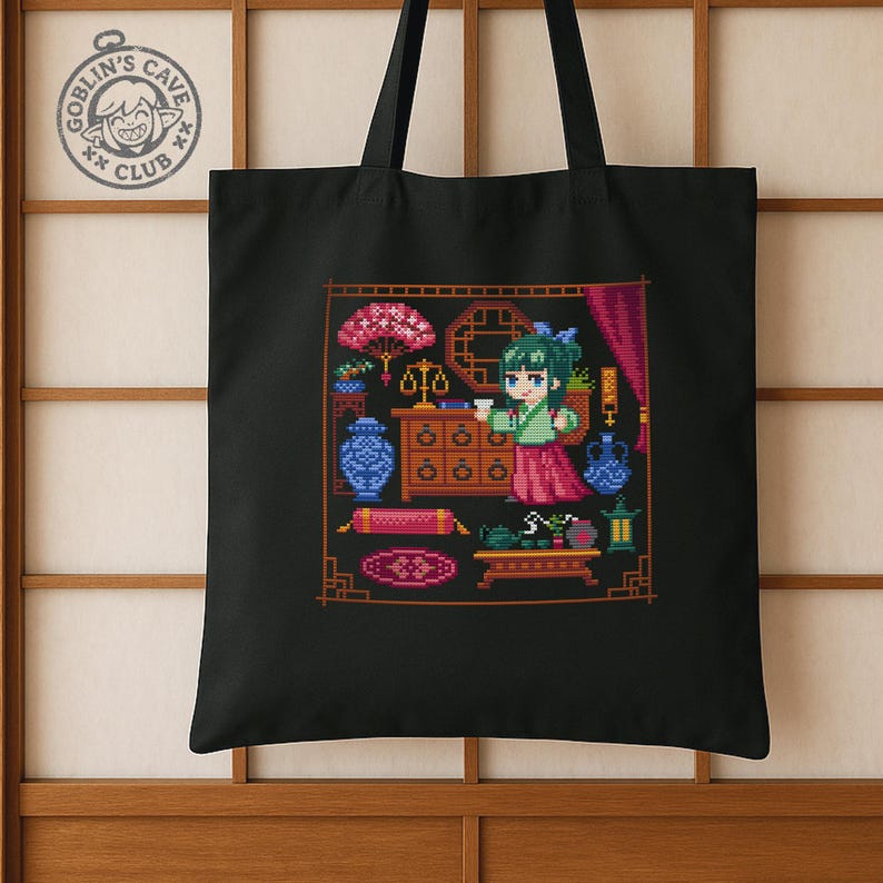 Puede incluir: Bolso tote negro con un dise&ntilde;o de pixel art de una mujer con vestimenta tradicional, rodeada de varios objetos. El dise&ntilde;o incluye una balanza, jarrones y un juego de t&eacute;. El bolso tambi&eacute;n tiene un logotipo circular que dice "Goblin's Cave Club".