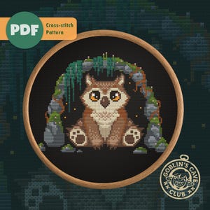 May include: A cross-stitch pattern featuring a brown owl with large orange eyes, sitting in a cave. The design is framed in a wooden hoop, with the text "PDF Cross-stitch Pattern" and "Goblin's Cave Club" visible.