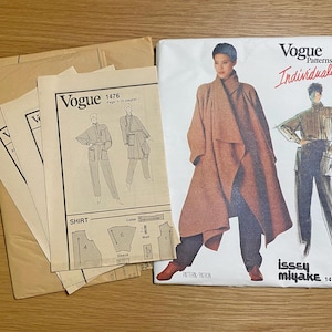May include: A collection of vintage Vogue sewing patterns. The main pattern features a woman in a long, draped coat and pants. The pattern is labeled "Vogue Patterns Individualist" and "Issey Miyake 1476". Several other pattern sheets are included.