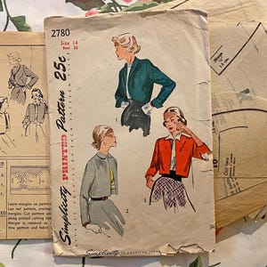 May include: A vintage Simplicity printed pattern envelope number 2780, size 14, bust 32. The beige paper envelope features illustrations of three jacket styles in teal, grey, and orange, along with printed text and internal paper pattern pieces.