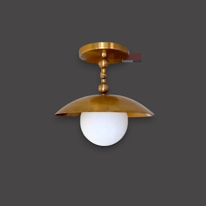 May include: A brass-colored ceiling light fixture with a white globe-shaped shade. The fixture has a round base and a curved shade. The text "MOD MIME" is visible on the fixture.