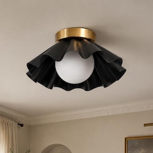 Può includere: Una plafoniera a incasso con un paralume in metallo nero opaco, ampio e ondulato. Il centro dell'apparecchio include una lampadina sferica in vetro bianco satinato fissata a una base circolare in metallo con finitura in ottone spazzolato.