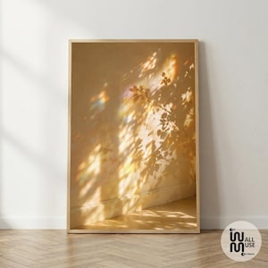 May include: A vertical rectangular framed art print featuring a warm, golden-toned wall surface with intricate shadows of tree branches and leaves cast across it, accented by soft, prismatic light refractions in shades of blue, pink, and yellow.