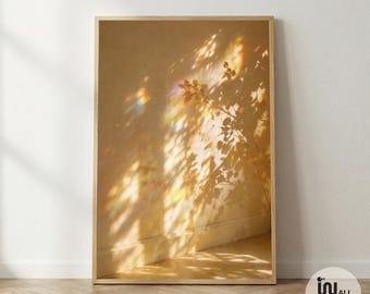 Op de afbeelding: Een verticale rechthoekige ingelijste kunstdruk met een warm goudkleurig muuroppervlak met ingewikkelde schaduwen van boomtakken en bladeren, geaccentueerd door zachte, prismatische lichtbrekingen in blauwe, roze en gele tinten.
