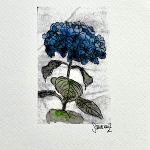 May include: A watercolor painting of a blue hydrangea flower with green leaves and stem. The artwork is on a white rectangular paper with a signature in the bottom right corner. The background is a light gray.