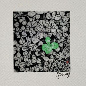 May include: A small art print with a detailed illustration of a field of clovers in black and white, with a single, vibrant green four-leaf clover in the centre. The artwork is signed in the lower right corner.