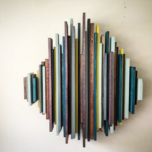 May include: Abstract wooden wall art composed of vertical, multi-colored wooden slats. The artwork features a diamond shape with various colors, including teal, yellow, gray, and brown, creating a modern, geometric design.