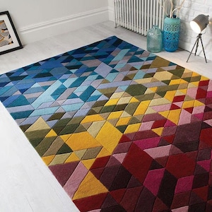 May include: A rectangular area rug with a geometric design. The rug features a gradient of colors, transitioning from blues and greens to yellows and reds. The pattern is composed of various-sized, angled shapes.