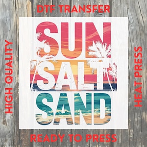 May include: A white DTF transfer with the words "SUN SALT SAND" in large, colorful letters. The design features a beach scene with palm trees and a sunset. The words "HIGH QUALITY" and "READY TO PRESS" are also visible.