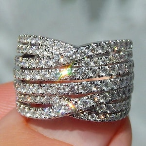 Op de afbeelding: Een sprankelende diamanten ring met meerdere rijen kleine, ronde diamanten. De ring heeft banden die elkaar kruisen, wat een uniek ontwerp creëert. De diamanten schitteren en vangen het licht, wat een opvallende glans geeft.