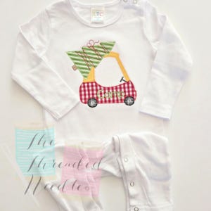 May include: White long-sleeved onesie with a Christmas-themed design. The design features a red and white checkered golf cart carrying a green Christmas tree with a red bow. The word "Camp" is embroidered on the cart.