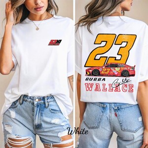Könnte beinhalten: Weißes T-Shirt mit Rennsport-Design. Auf der Vorderseite befindet sich ein kleines Logo, während die Rückseite die Nummer 23, eine Rennwagen-Grafik und den Namen "Bubba Wallace" zeigt. Das Shirt wird mit Jeansshorts getragen.
