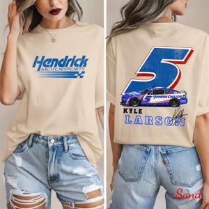May include: Beige t-shirt featuring the "Hendrick Motorsports" logo in blue and white on the front. The back of the shirt displays a large blue number 5 with a race car graphic and "Kyle Larson" text.