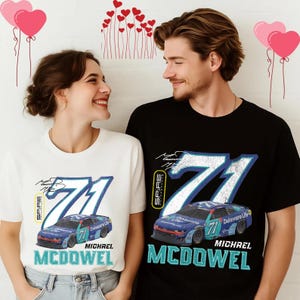 May include: White and black t-shirts featuring a racing car design with the number 71 and the name "MICHAEL MCDOWELL". The shirts have a vintage aesthetic, with a blue and white color scheme. The word "SPIRE" is also visible.