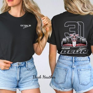 Op de afbeelding: Donkergrijs t-shirt met de tekst "OCON 31" op de voorkant. De achterkant van het shirt heeft een Formule 1-auto-afbeelding, het nummer "31" en de naam "ESTEBAN OCON".